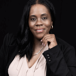 Principal Kristin Johnson – Add B. Anderson School Principal Kristin Johnson of Add B. Anderson School, wearing a black blazer and light blouse, smiling and resting her hand under her chin against a black background.